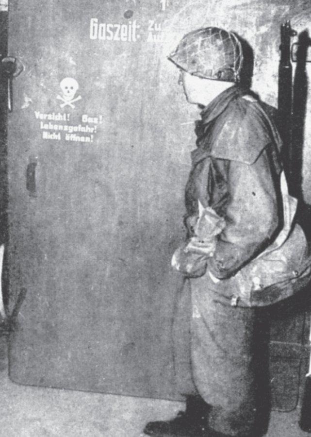 Alliierter Soldat nach Kriegsende vor einem Gaskammereingang im KZ.