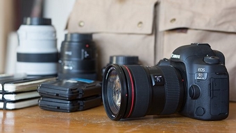 A Male with a tattooed hand in an outdoors environment with a Canon DSLR handing on his side
