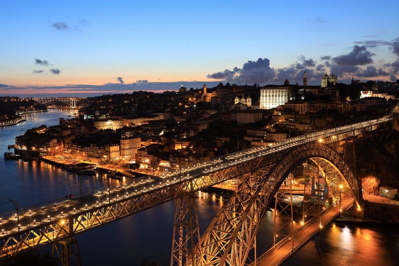 An expansive cityscape, including a winding river and brightly-lit road bridge, shot using a Canon EOS R at sunset and filled with the artificial lights of the city and traffic.