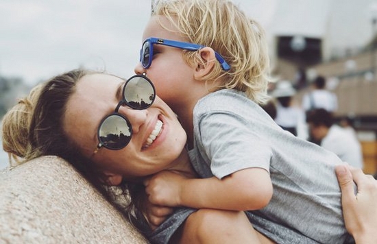 A mother picks her son up to hug, both of them wearing sunglasses.