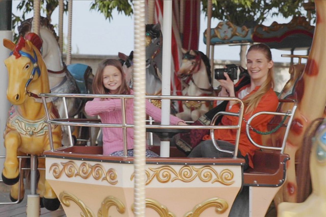 A woman with a Canon EOS 250D rides a carousel with her daughter.