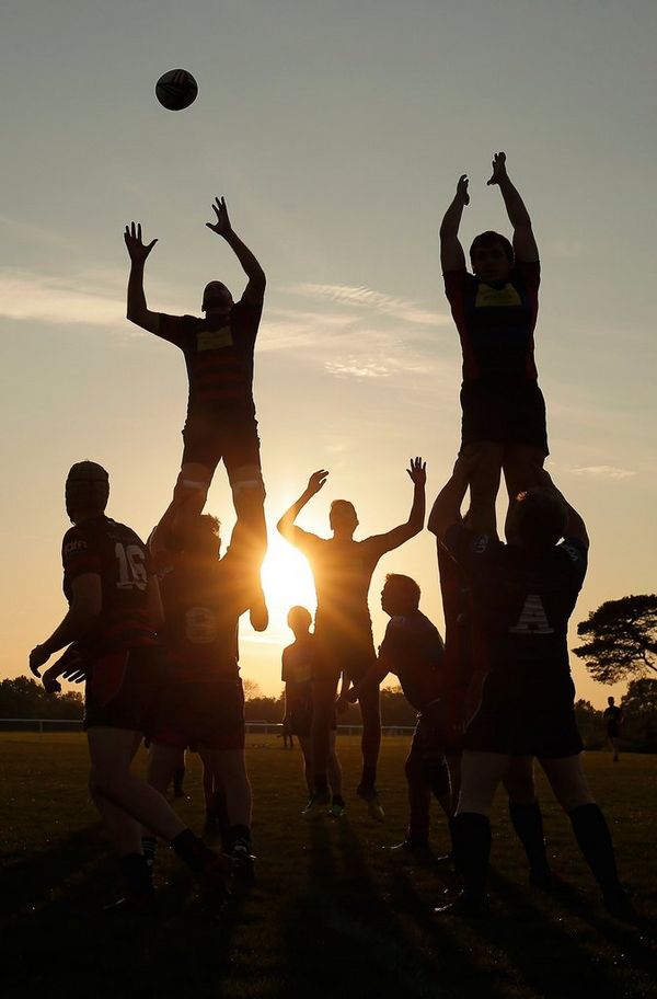 Silhouette of rugby players jumping for a ball at sunset. Photo by Tom Jenkins.