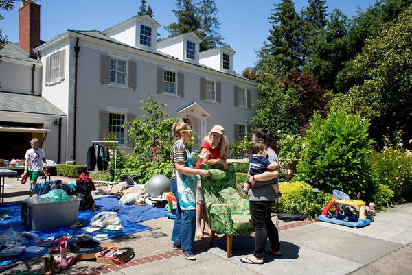 Three women talk at a garage sale in front of a large house. Photo by Laura Morton.