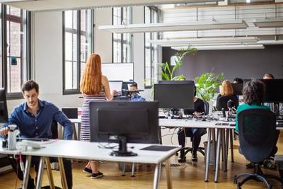 Woman with long ginger hair works at a standing desk amongst colleagues 