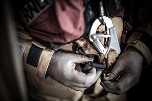 A close-up shows a volunteer’s hands fastening a harness over their yellow sailing gear and red life vest.