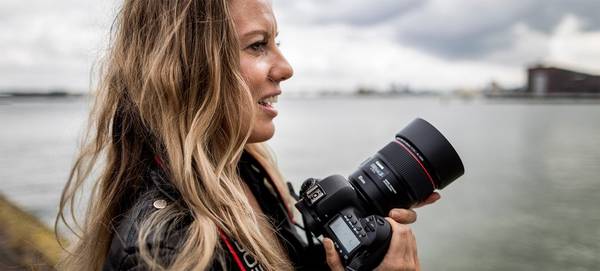 Photographer Ilvy Njiokiktjien stands in front of a harbour holding a Canon DSLR.