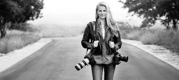 Photographer Elizabeth Kreutz stands in the middle of a road with two Canon cameras over her shoulders.