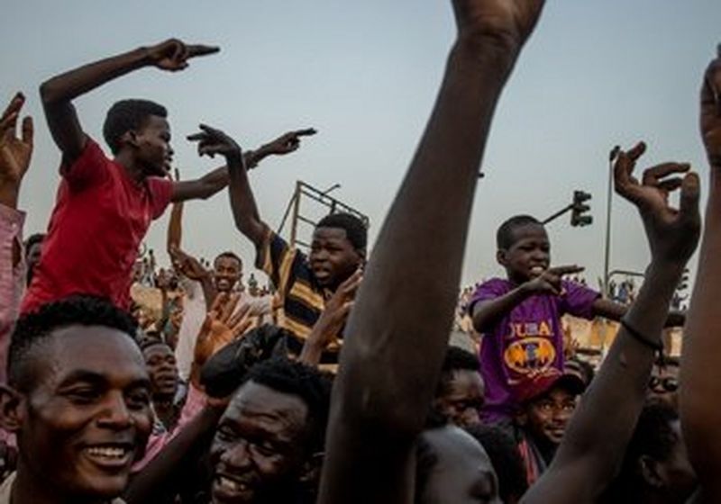 A crowd of closely packed people smiling with their arms raised.