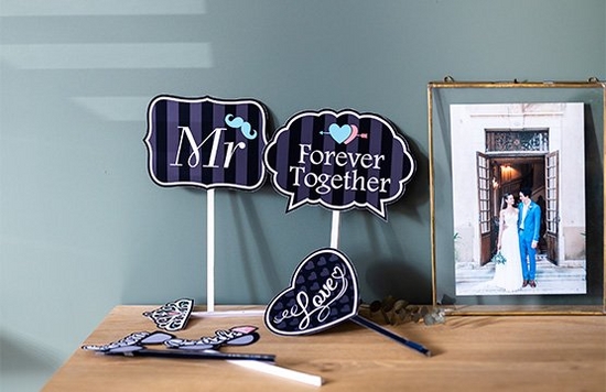 Printed decorations and hand-held signs for a wedding day next to a portrait of a bride and groom in a frame.