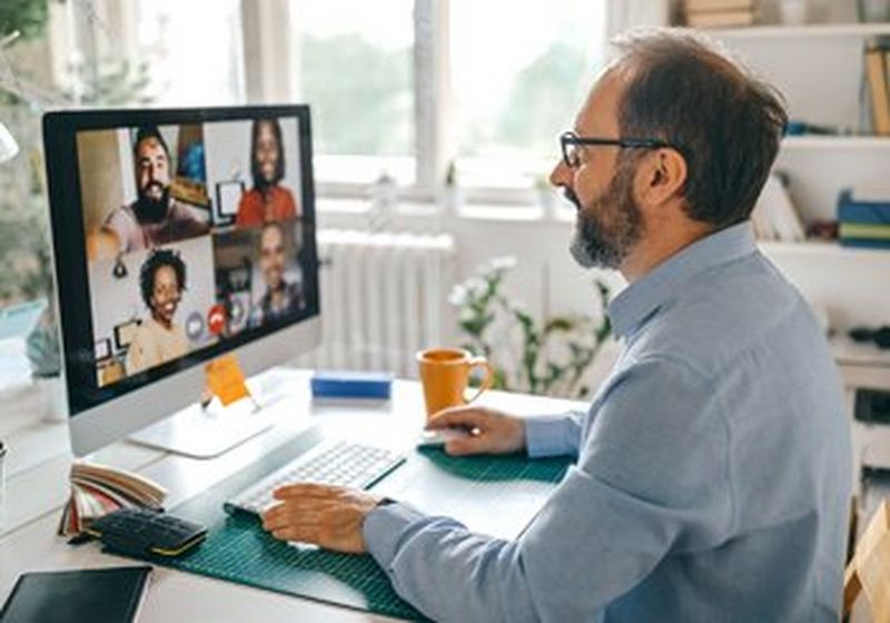 A bearded and bespectacled man sits in his home office, at his computer. He is on a conference call with four other people.