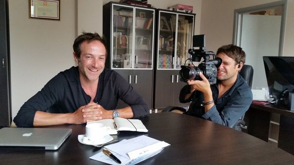 DOP Jake Swantko pointing a videocamera at Bryan Fogel while both sit at a table.
