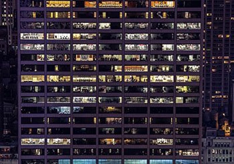 A building, photographed from the outside at night, showing dozens of lit offices.