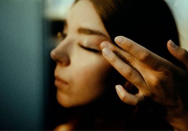 A portrait of a woman from the side. She stretches the skin on her left eye with her fingers.