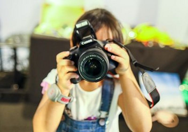 A child holds a Canon camera, obscuring his/her face