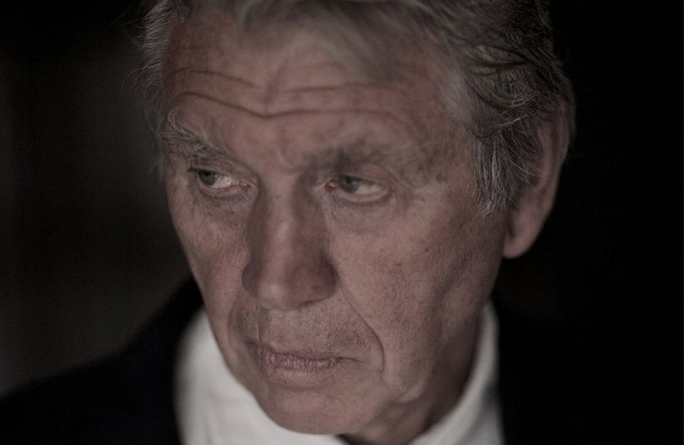 Sir Don McCullin, dressed in a white shirt and black jacket, poses for a portrait shot. 