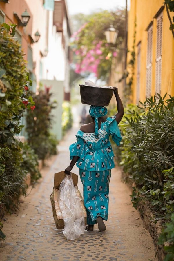 A woman wearing a patterned turquoise outfit, walking down an alley on Gorée Island, Senegal.