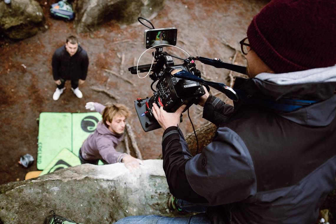Filmmaker Nicolai Deutsch kneels on the edge of a ledge filming two rock climbers with a Canon EOS C500 Mark II. 
