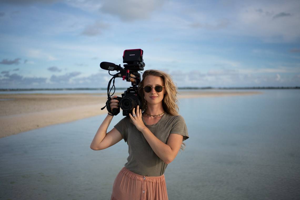 Filmmaker Alice Aedy on the coast of Kiribati holding a Canon EOS C300 Mark II.