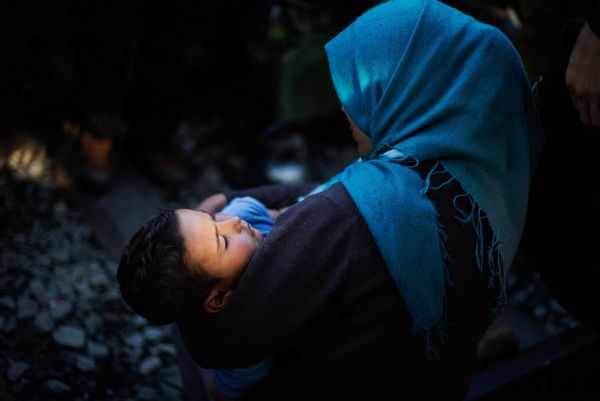 A Syrian woman in a blue headscarf cradles a child at the Idomeni refugee camp in Greece.