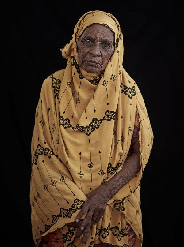 A portrait taken in rural Somaliland of an elderly woman in a yellow patterned dress.