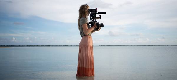 Filmmaker Alice Aedy standing in the sea holding a Canon EOS C300 Mark II.
