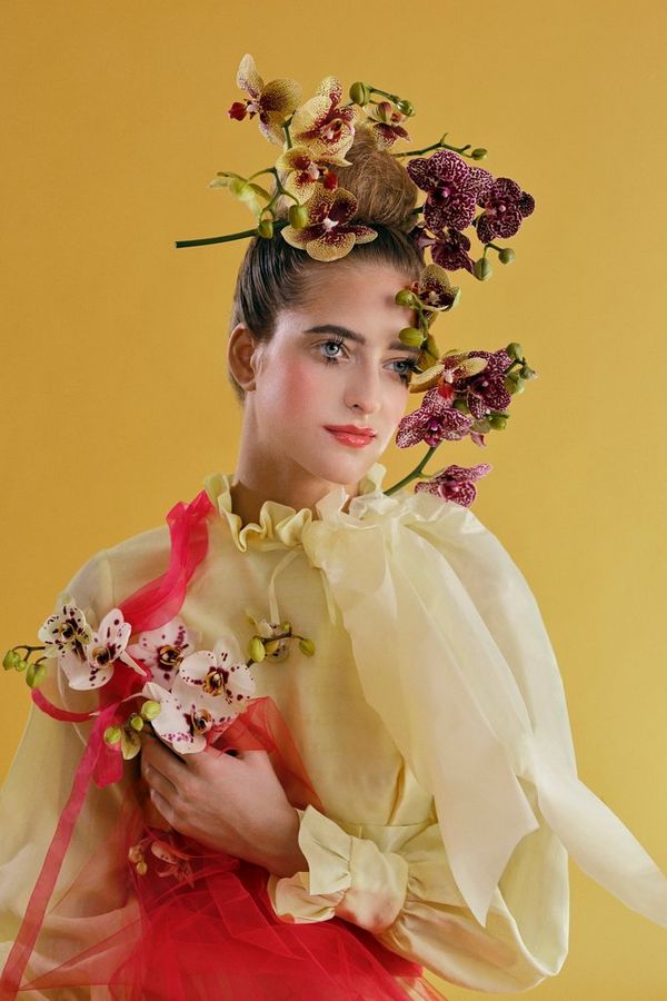 A model wearing pastel yellow and pink lace holding flowers.