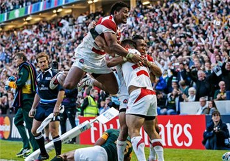 Japan's Karne Hesketh celebrates with team mates at the corner of a rugby pitch with cheering crowd in the background