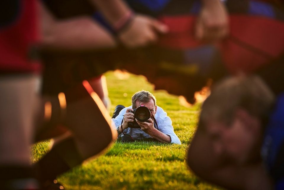 A photographer lies on the ground to photograph a rugby scrum.