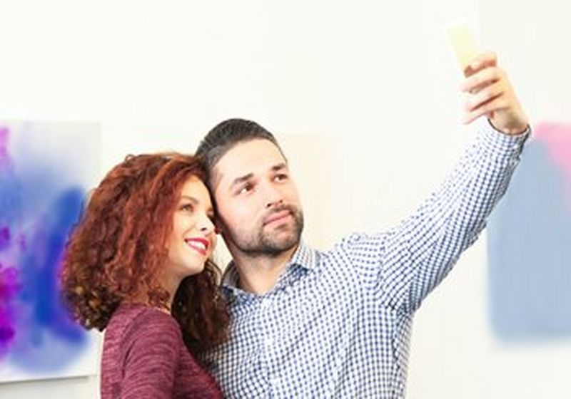 A couple take a selfie in front of a piece of modern art