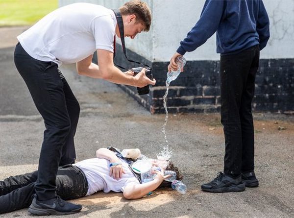 A schoolgirl lies on the floor having water poured over her face