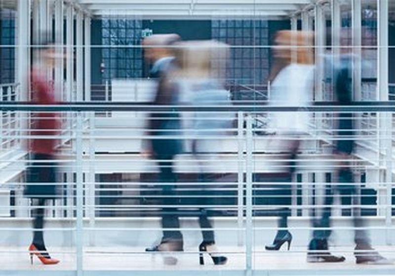 Blurred figures crossing an office walkway.