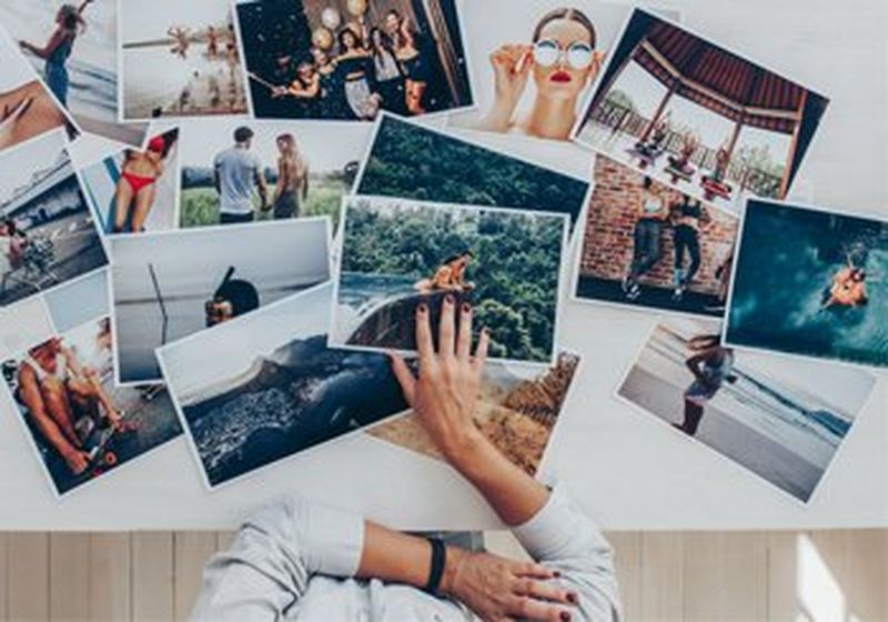 A top down view of a table, with photographs spread all over it, and a pair of hands about to select one.