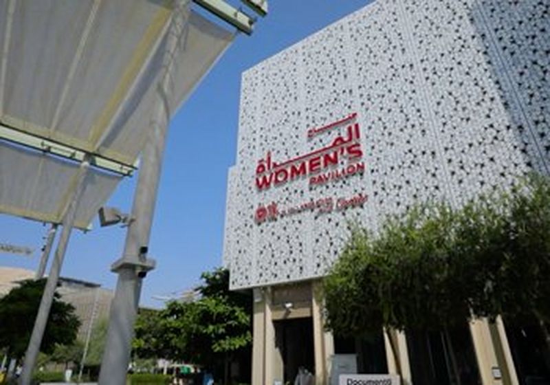 The front of the Women's Pavilion at Expo 2020 Dubai. It is a white tiled building that appears to be on stilts. It has a red-lettered sign saying 'women's pavilion' on the front. 