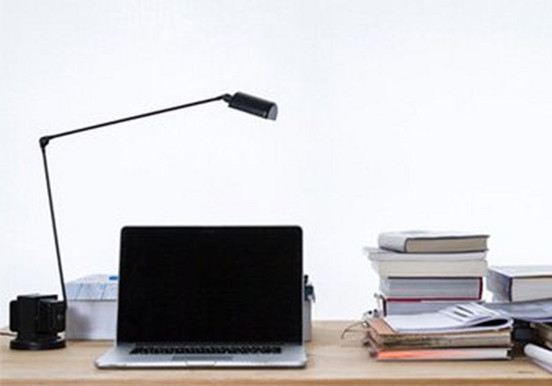 A wooden desk, with a stack of piled books beside a laptop.