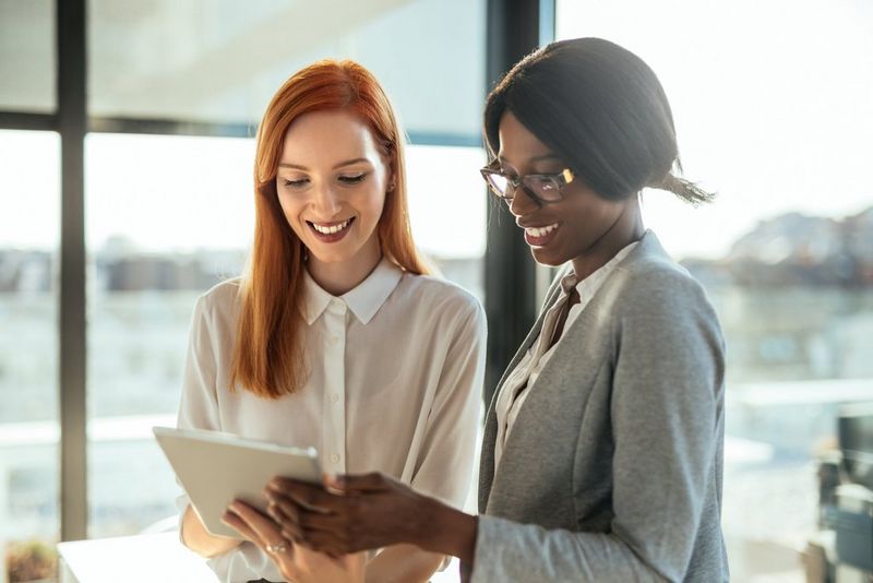 Two office professionals smiling and holding a tablet