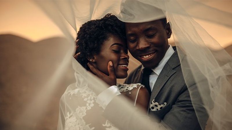 A couple wearing wedding apparel embracing and smiling.
