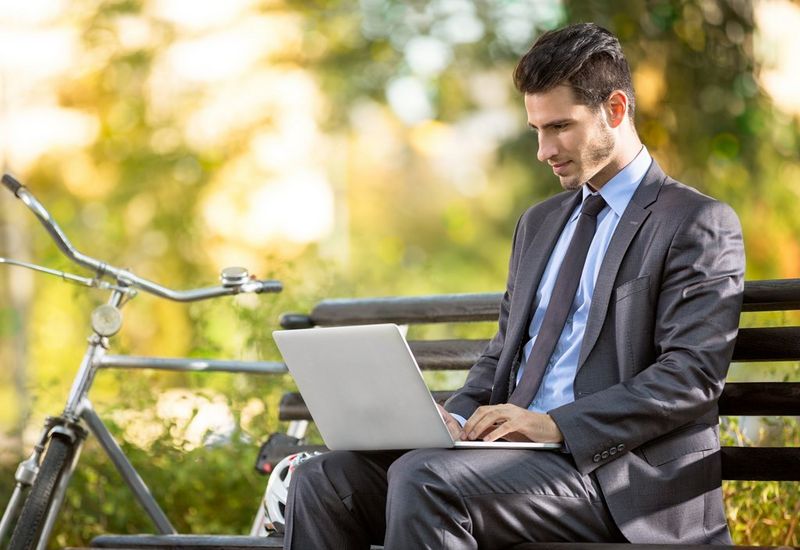 a man sitting on a bench working on laptop