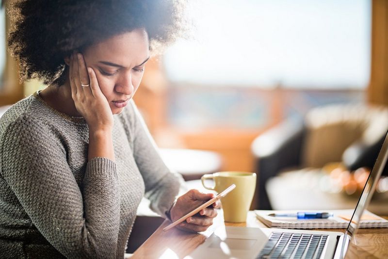 Woman sitting by a desk looking at her phone with a sad look on her face