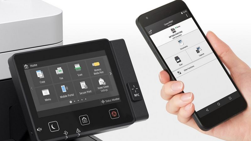 A woman holding a smartphone in her hand showing the app. A large office printer is in the background.  