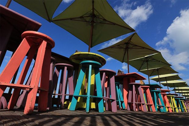 An array of colourful wooden stools, with square-shaped sunshades above, photographed from ground level looking up, on a Canon EOS 250D.