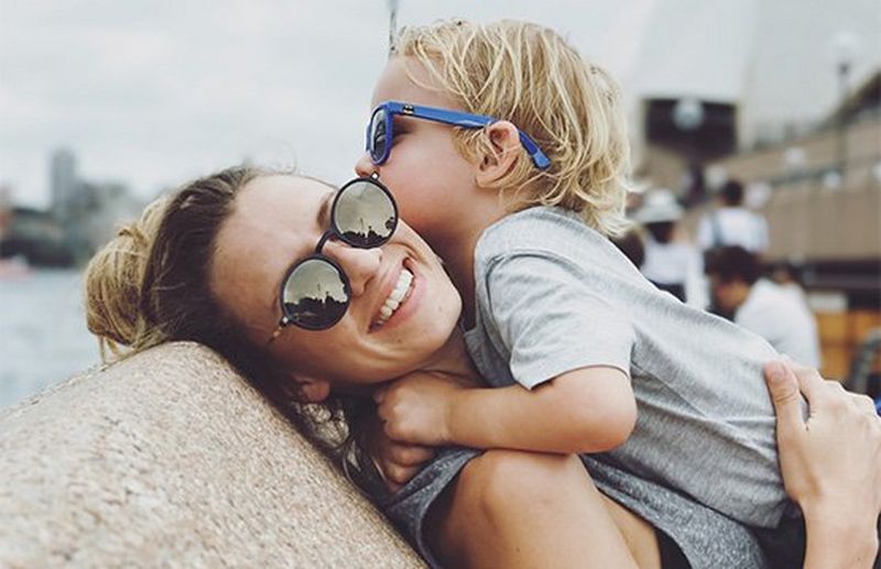 A mother picks her son up to hug, both of them wearing sunglasses. Photo by Christian Anderl.