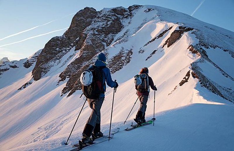 Two cross-country skiers travel along the narrow spine of a mountain, using their poles. Winter sports photo by Richard Watch.