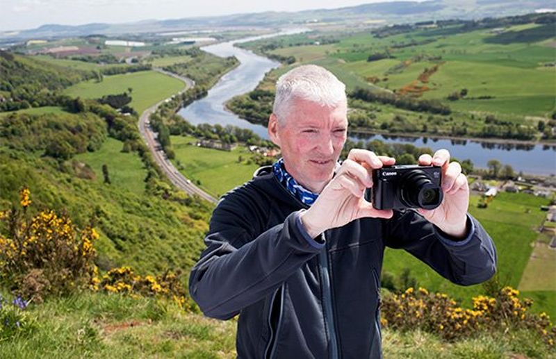 Alan Rowan holds a Canon PowerShot SX740 HS camera to take a landscape photograph.