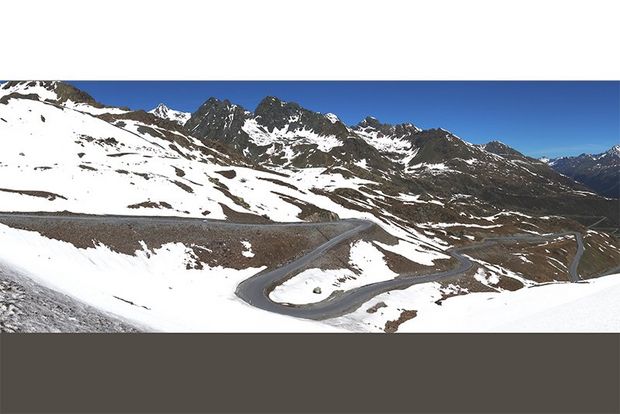 A panoramic shot of a winding road by snowy mountains.