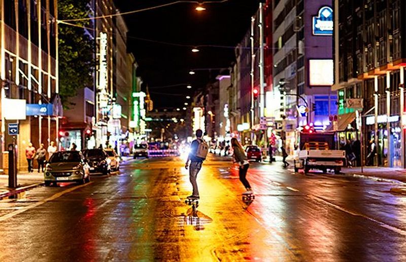 Two young people skateboard down a city street at night.