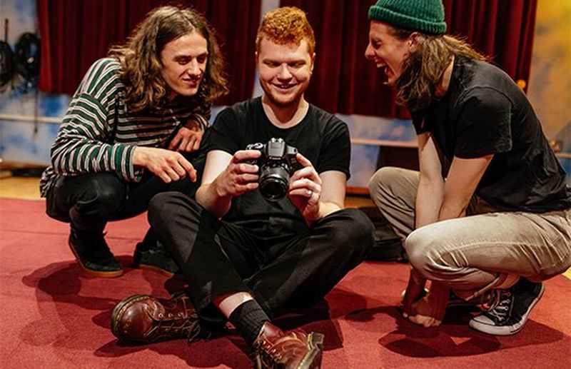 Music photographer Josh Gibbs holds a Canon EOS 2000D with two young men beside him.