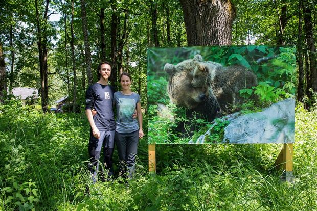 Christine and Marc stand by a printed version of one of their shots displayed as part of an outdoor exhibition in a forest.