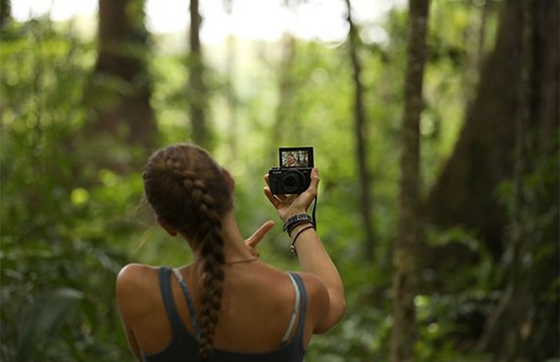Laura Bingham pictured from behind, facing dense jungle, as she films a vlog with a Canon PowerShot G7 X Mark II.