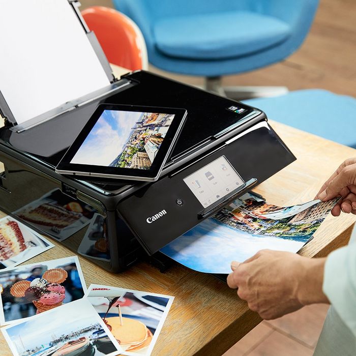 Hands taking prints from a Canon printer; a tablet on top showing a printing app.