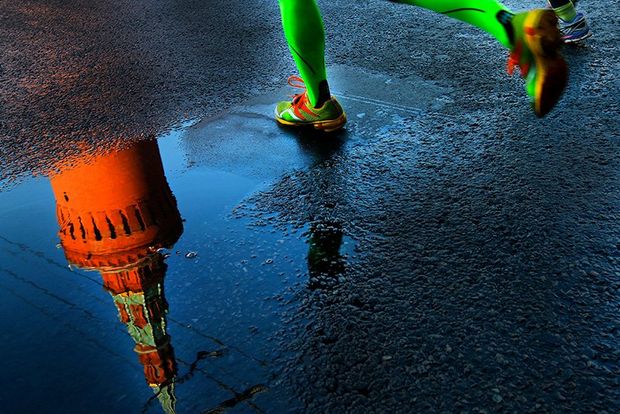 A tower of the Kremlin reflected in a puddle as a runner with bright green socks runs past. Photo by Andrey Golovanov.